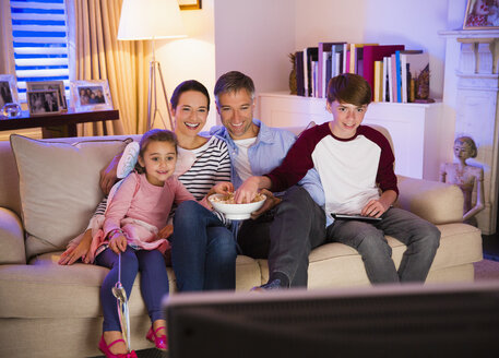 Familie isst Popcorn und sieht im Wohnzimmer fern - CAIF11884