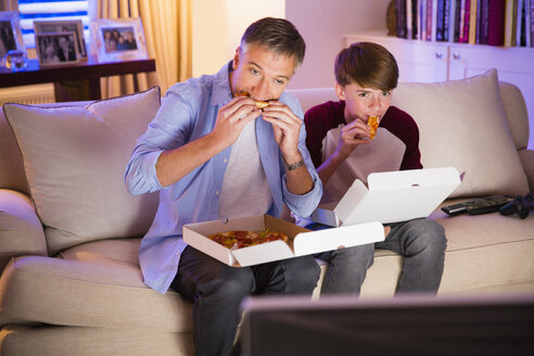 Vater und Sohn essen Pizza und sehen im Wohnzimmer fern - CAIF11887