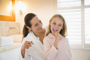 Mother and daughter brushing teeth in bathroom - CAIF11890