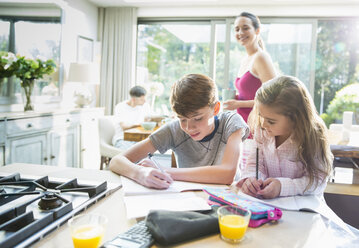 Mutter beobachtet Bruder und Schwester bei den Hausaufgaben am Küchentisch - CAIF11894