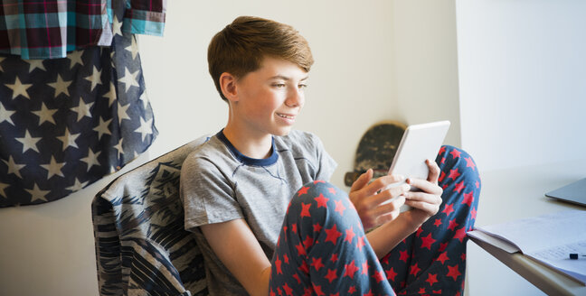 Junge im Pyjama mit digitalem Tablet im Schlafzimmer - CAIF11896