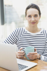 Portrait confident woman drinking coffee at laptop - CAIF11908