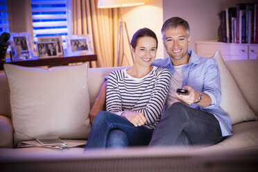 Lächelndes Paar beim Fernsehen im Wohnzimmer - CAIF11913
