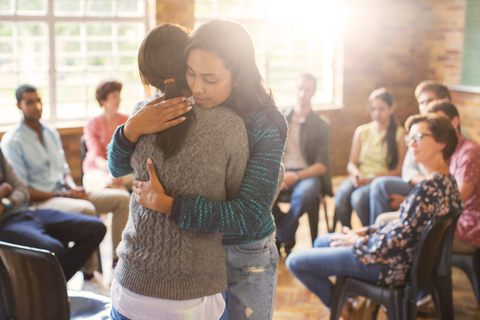 Frauen umarmen sich in einer Gruppentherapiesitzung, lizenzfreies Stockfoto