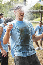 Enthusiastischer Mann genießt Wasserschlauchspritzen auf Bootcamp-Hindernisparcours - CAIF12001