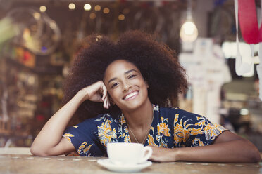 Porträt einer lächelnden Frau mit Afro, die in einem Café Kaffee trinkt - CAIF12090