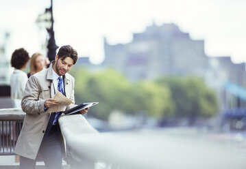 Businessman reading newspaper on urban waterfront - CAIF12099