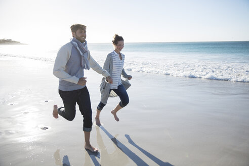 Junges Paar hält sich an den Händen und läuft am Strand - CAIF12132