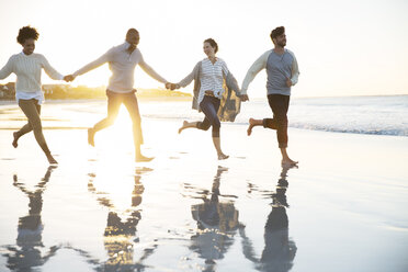 Gruppe von vier Freunden, die sich an den Händen halten und am Strand laufen - CAIF12134