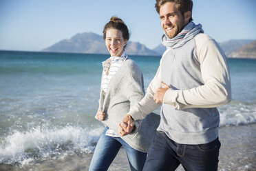 Young couple holding hands and walking on beach - CAIF12141