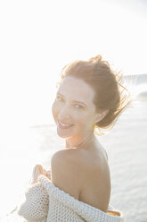 Portrait of young woman wrapped in blanket on beach - CAIF12144