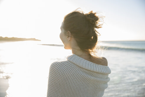 Junge Frau in Decke eingewickelt am Strand - CAIF12146