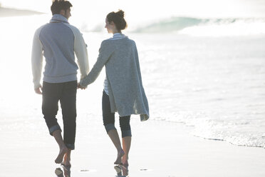 Young couple holding hands and walking on beach - CAIF12153