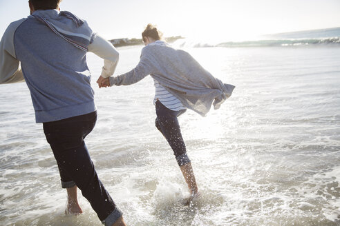 Junges Paar hält sich an den Händen und läuft am Strand - CAIF12154