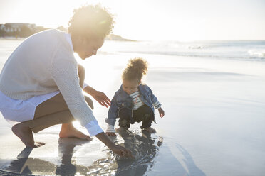 Mother and daughter drawing on wet sand on beach - CAIF12155