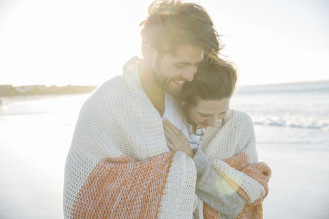 Junges Paar in Decke eingewickelt am Strand, lizenzfreies Stockfoto