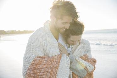 Junges Paar in Decke eingewickelt am Strand - CAIF12157