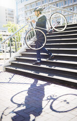 Businessman in suit and helmet carrying bicycle down urban stairs - CAIF12172