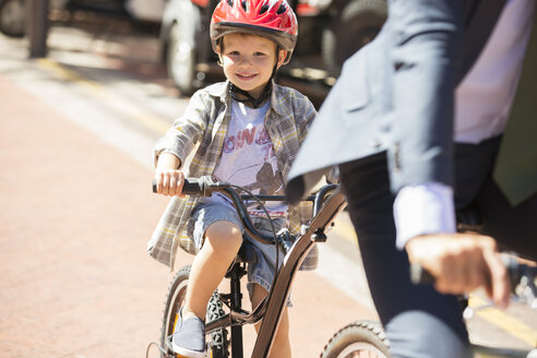 Portrait lächelnder Junge auf dem Fahrrad auf einer sonnigen Straße - CAIF12174