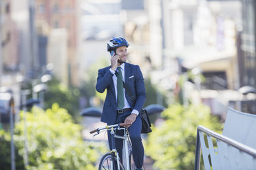 Geschäftsmann in Anzug und Helm, der auf einem Fahrrad sitzt und mit einem Handy in der Stadt telefoniert - CAIF12177