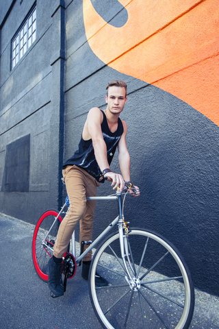 Porträt ernster junger Mann auf Fahrrad neben städtischer Graffiti-Wand, lizenzfreies Stockfoto