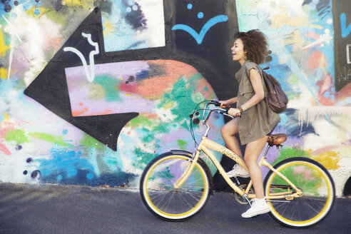 Frau fährt mit dem Fahrrad entlang einer städtischen mehrfarbigen Graffiti-Wand - CAIF12185