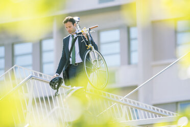 Businessman in suit carrying bicycle in city - CAIF12187