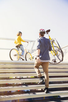 Mann mit Helm, der ein Fahrrad eine Treppe hinauf trägt - CAIF12193