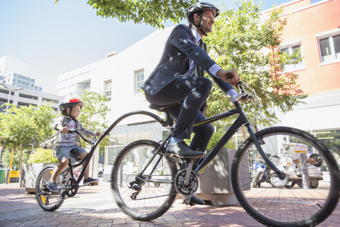 Geschäftsmann, Vater im Anzug, fährt mit seinem Sohn auf einem Tandemfahrrad auf einem städtischen Bürgersteig - CAIF12195