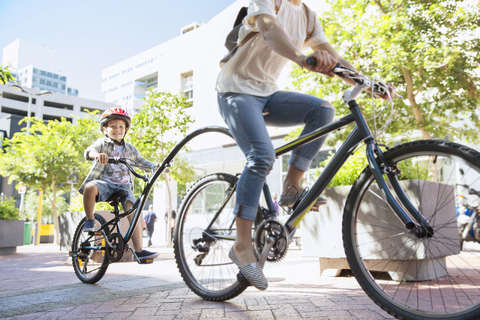 Sohn mit Helm fährt Tandem mit Mutter in einem Stadtpark, lizenzfreies Stockfoto