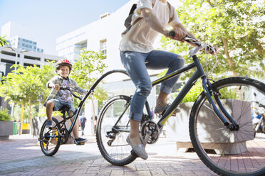 Sohn mit Helm fährt Tandem mit Mutter in einem Stadtpark - CAIF12198