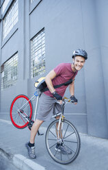 Porträt eines lächelnden Fahrradkuriers mit Helm, der sich auf einem städtischen Bürgersteig nach vorne lehnt - CAIF12203