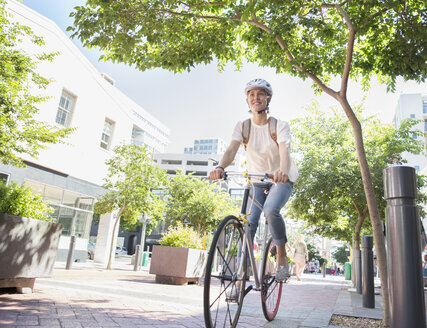 Lächelnde junge Frau mit Helm auf dem Fahrrad in einem Stadtpark - CAIF12204