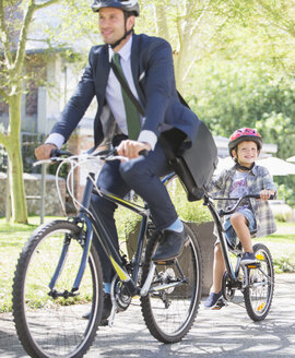 Geschäftsmann in Anzug und Helm fährt mit Sohn auf einem Tandemfahrrad - CAIF12205