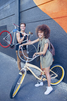 Porträt lächelnd Freunde mit Fahrrädern neben städtischen Wand - CAIF12208