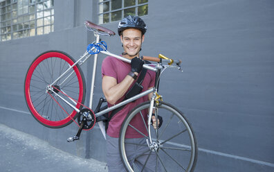 Portrait smiling young man carrying bicycle on urban sidewalk - CAIF12209