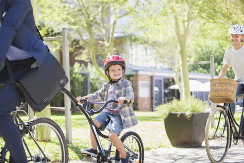 Porträt eines lächelnden Jungen mit Helm, der mit seinem Vater im Park Tandem fährt - CAIF12210