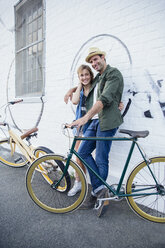 Porträt lächelnd Paar mit Fahrrädern umarmen an städtischen Wand - CAIF12213