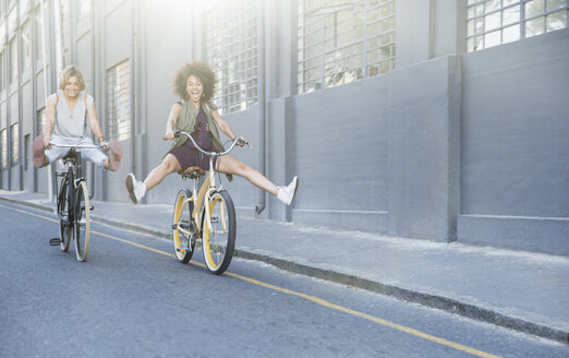 Verspielte Frauen, die auf Fahrrädern durch die Stadt fahren - CAIF12214
