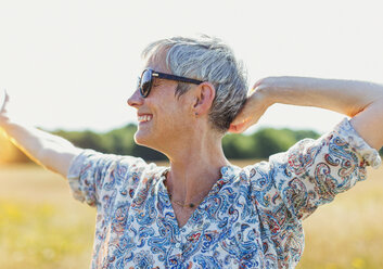 Enthusiastische ältere Frau mit ausgestreckten Armen in einem sonnigen Feld - CAIF12216