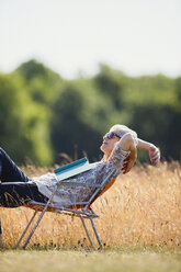 Carefree senior woman relaxing with book in sunny field - CAIF12218