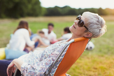 Ältere Frau entspannt sich auf einem Stuhl in einem Feld - CAIF12226