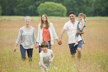 Mehrgenerationen-Familie, die sich an den Händen hält und auf einem ländlichen Feld spazieren geht - CAIF12230