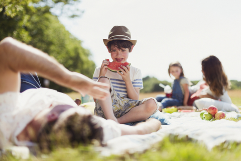 Smiling boy eating watermelon on blanket in sunny field stock photo