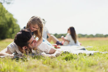 Affectionate daughter laying on top of father in sunny field - CAIF12275