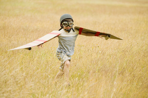 Junge mit Flügeln, Fliegermütze und Fliegerbrille auf einem Feld laufend - CAIF12289