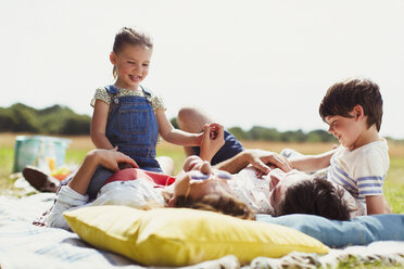 Family relaxing on blanket in sunny field - CAIF12298