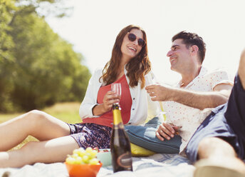 Ehepaar trinkt Champagner auf einer Picknickdecke in einem sonnigen Feld - CAIF12302