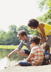 Family playing with toy sailboat at lakeside - CAIF12306