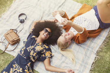 Friends taking selfie relaxing on blanket in grass - CAIF12323